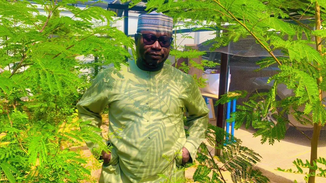 A man standing among young trees with feathery green leaves in a planted enclosure.