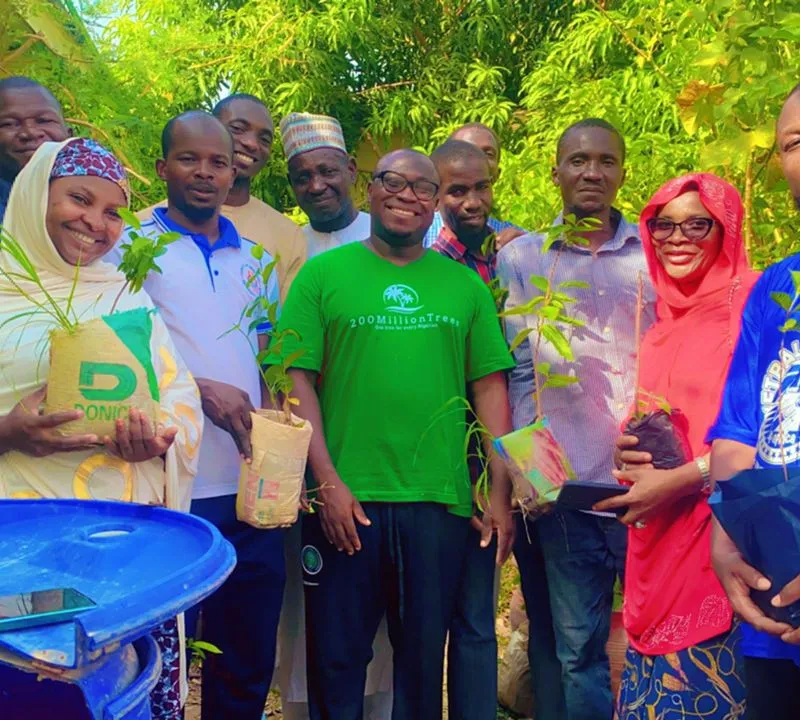 A group of men and women standing together outdoors, each holding a tree seedling ready for planting.