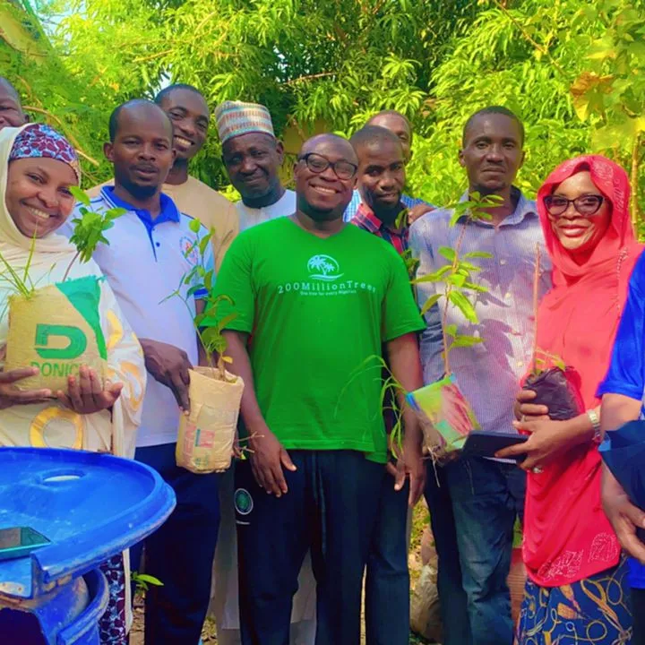 A group of men and women standing together outdoors, each holding a tree seedling ready for planting.